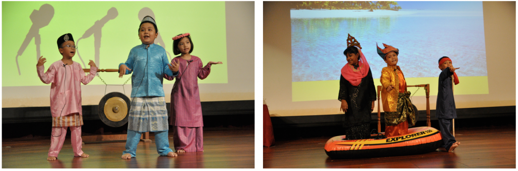 Children in traditional Malay costumes perform on stage, one group near a gong, another standing in an inflatable boat.